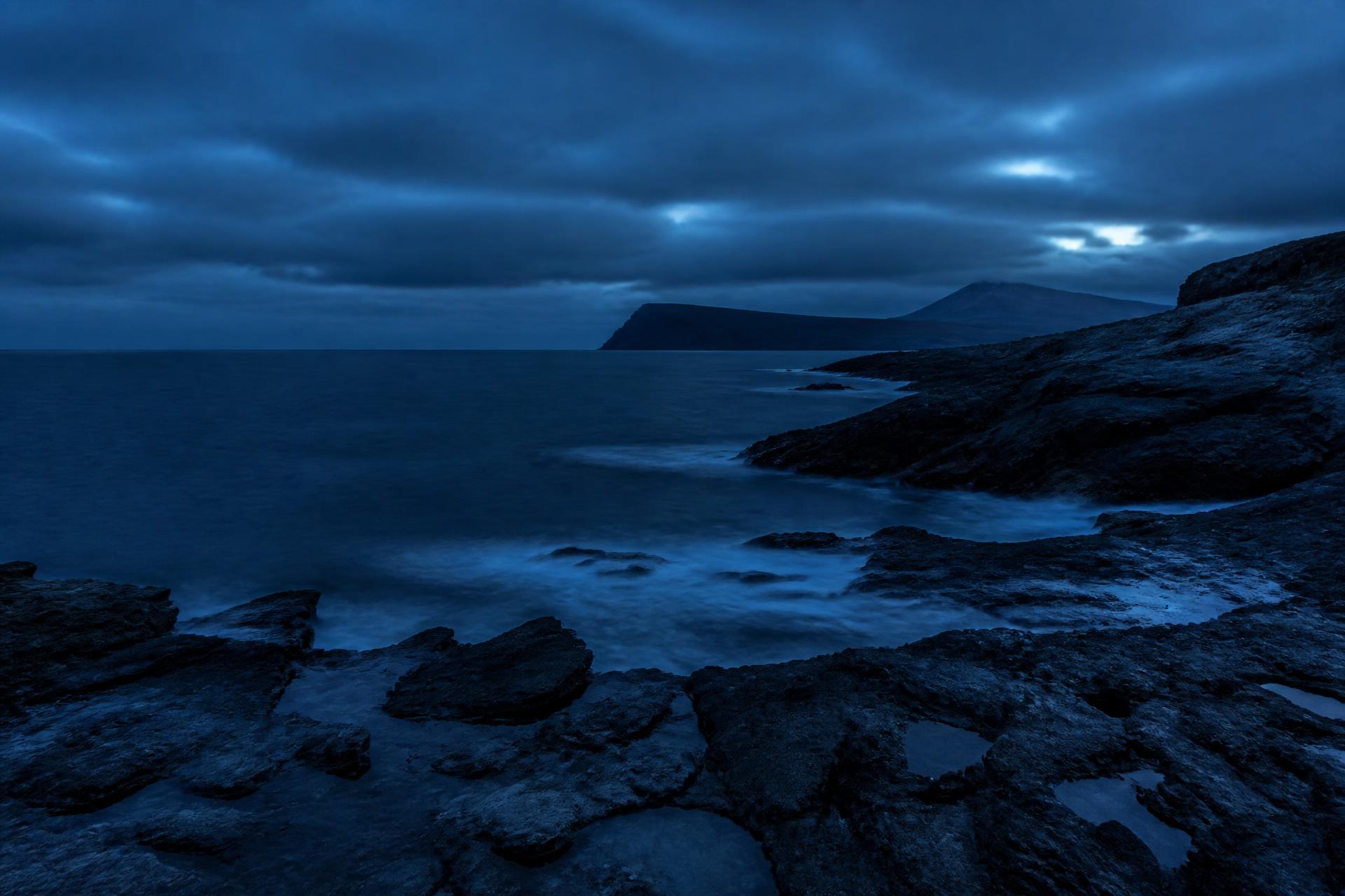 Cold rocky coastline at dusk, graded deep navy blue